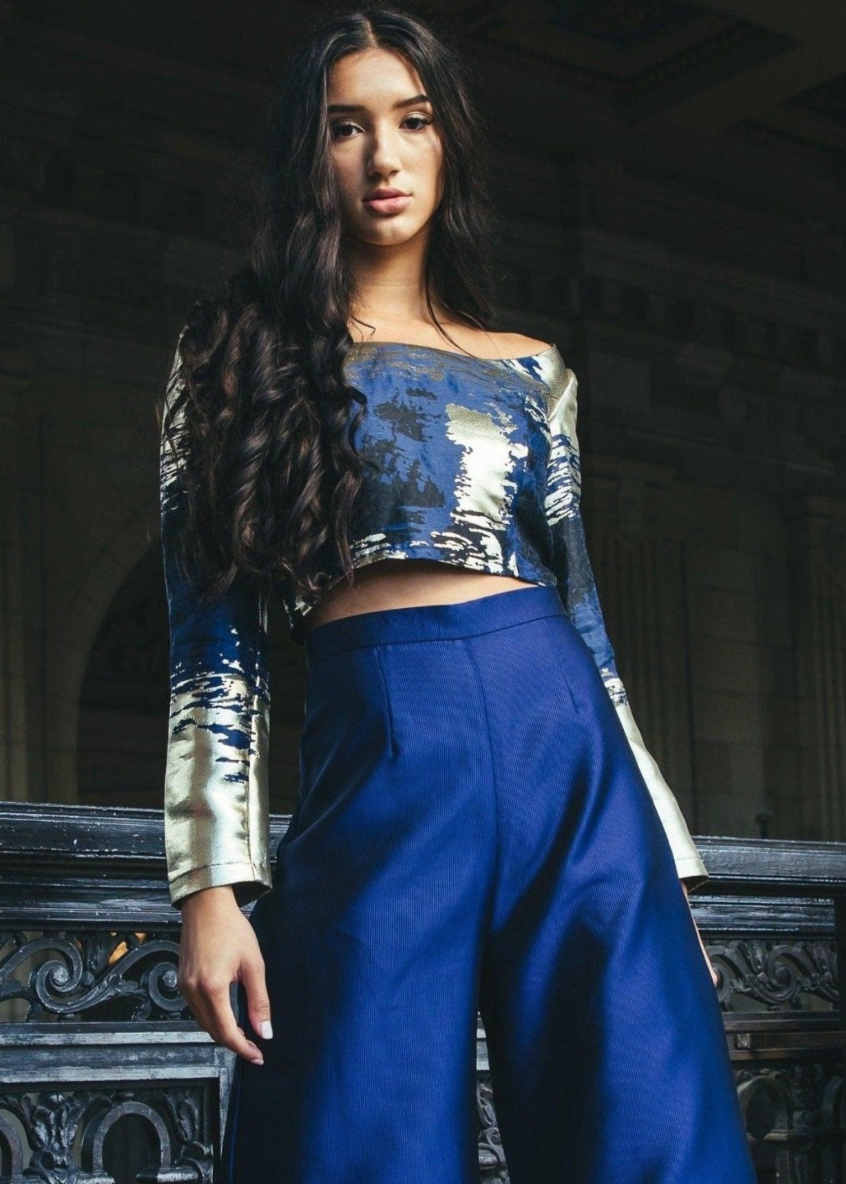 The 'Zendaya Top' paired with blue pants modeled by a woman on a balcony