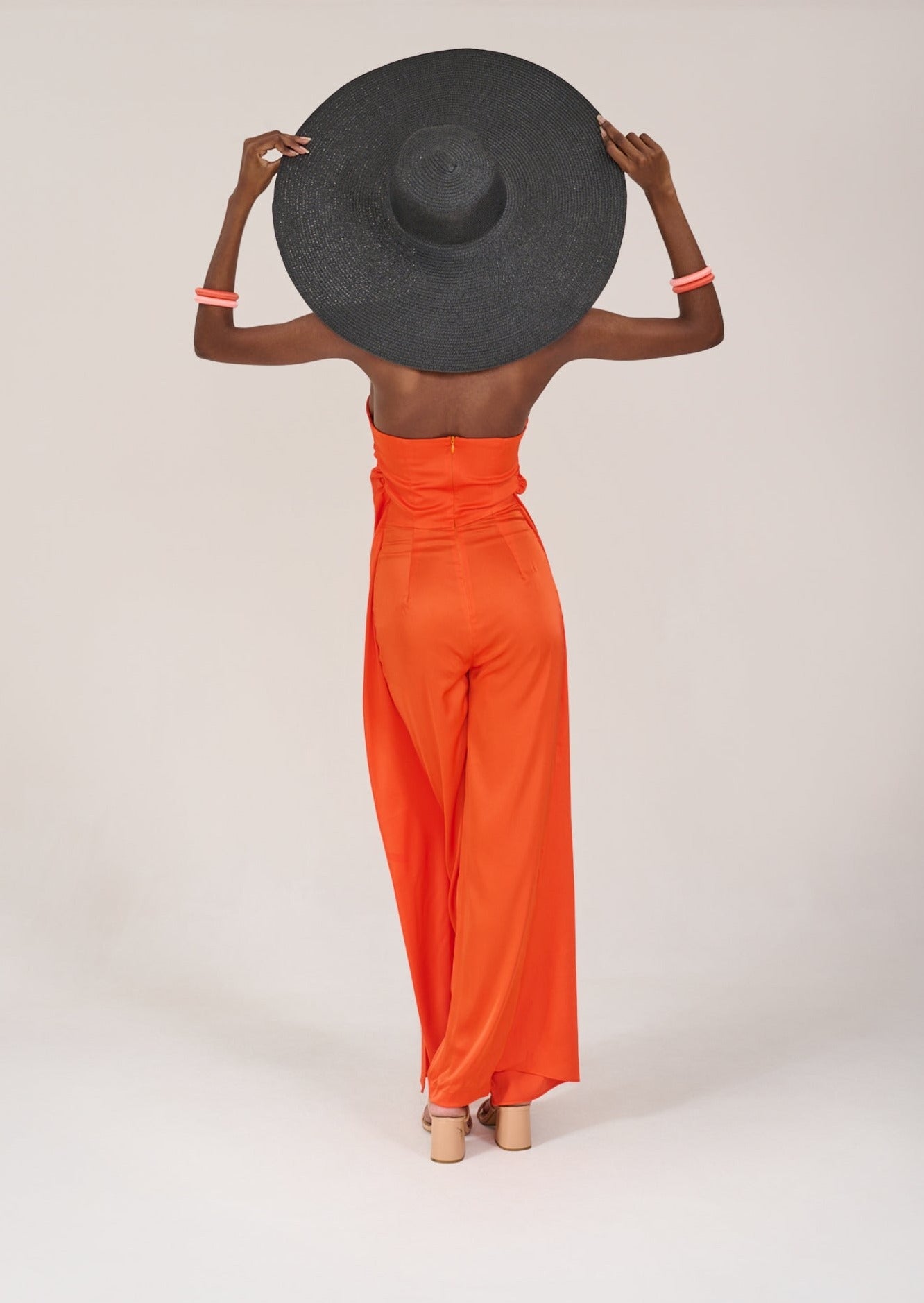 Model facing backwards, wearing the KAHINDO Imizamo Jumpsuit, styled with a black wide brim straw hat
