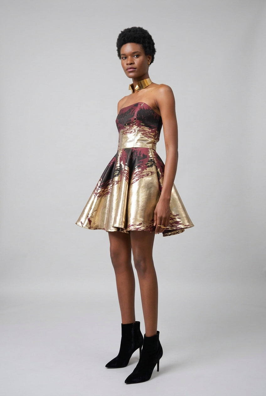 Model wearing a gold and floral dress with black high-heeled boots against a white curtain background
