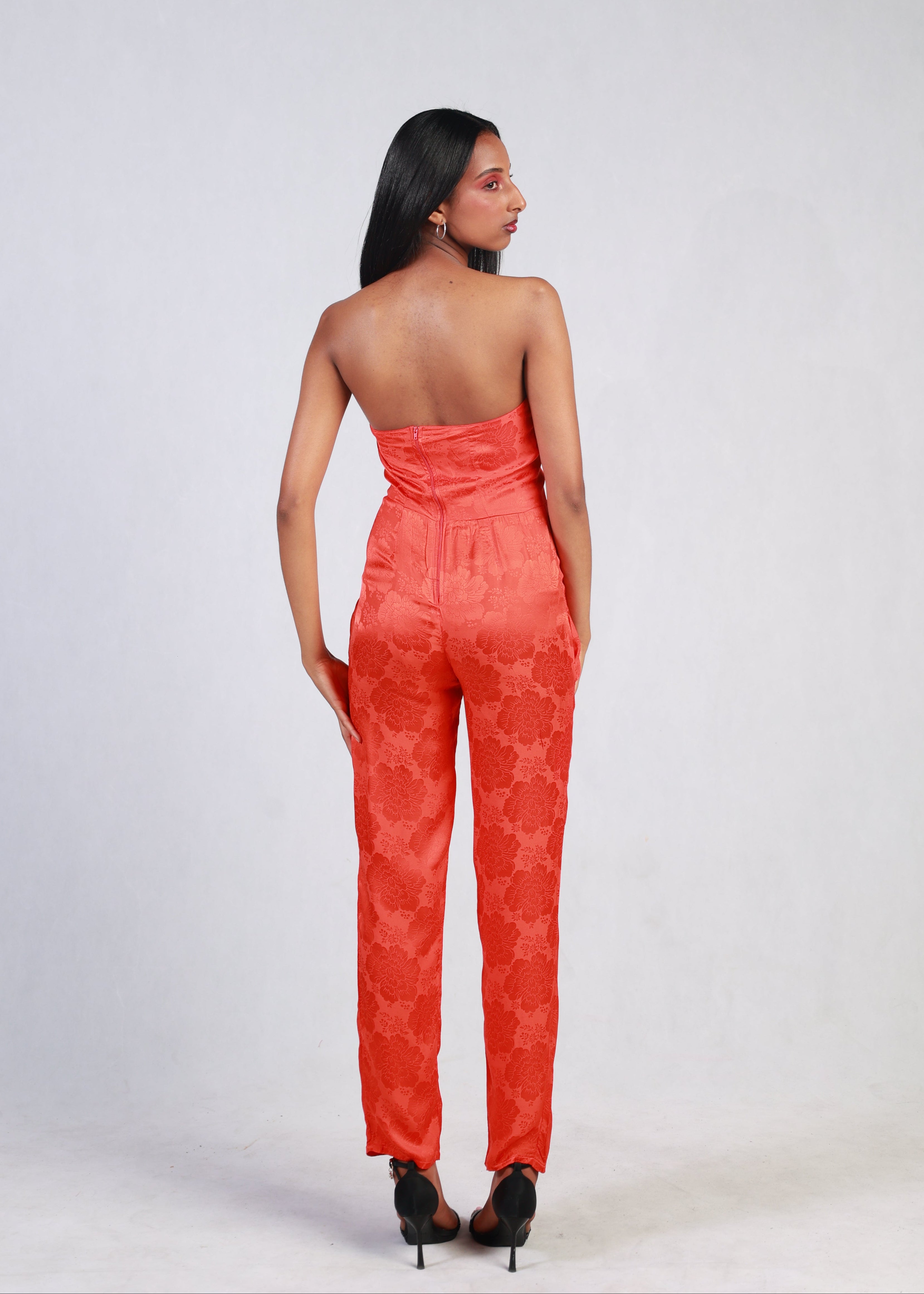Woman wearing a red strapless jumpsuit against a white background