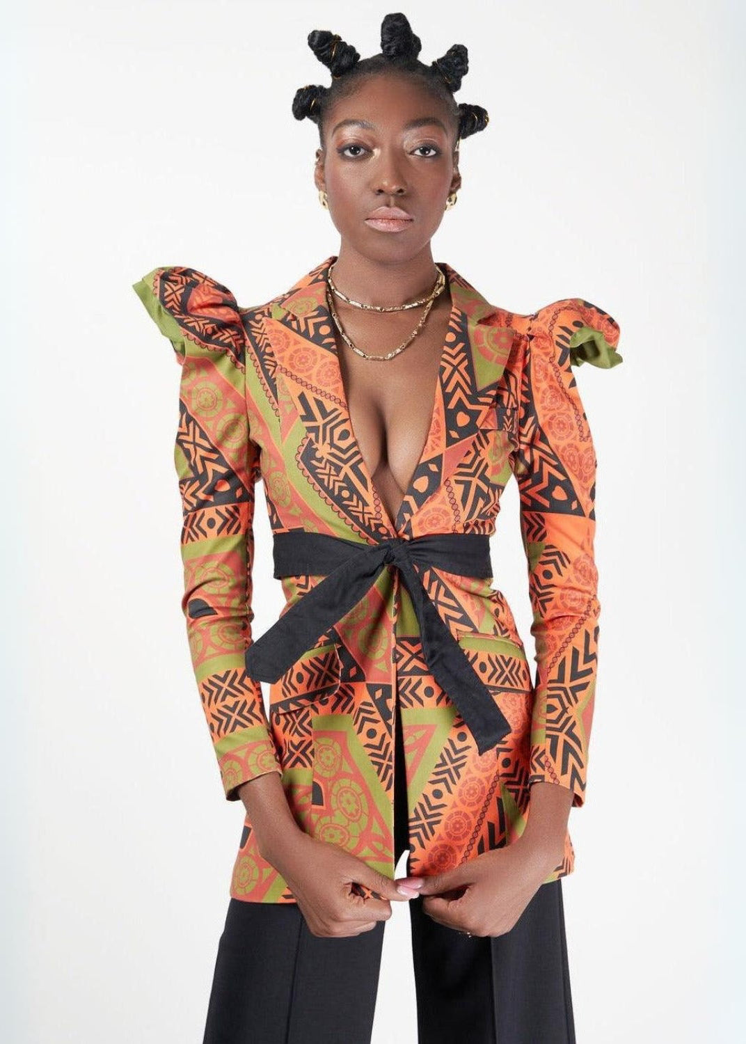 Tanganyika Jacket in vibrant African print featuring dramatic puff shoulders, a deep V-neckline, black waist tie, and tailored silhouette, styled with black wide-leg pants in a studio setting.