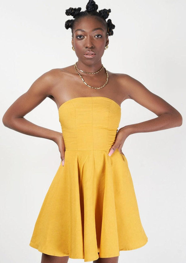 A model showcasing the 'Mweru Mini Dress' in yellow with a strapless top and pleated skirt