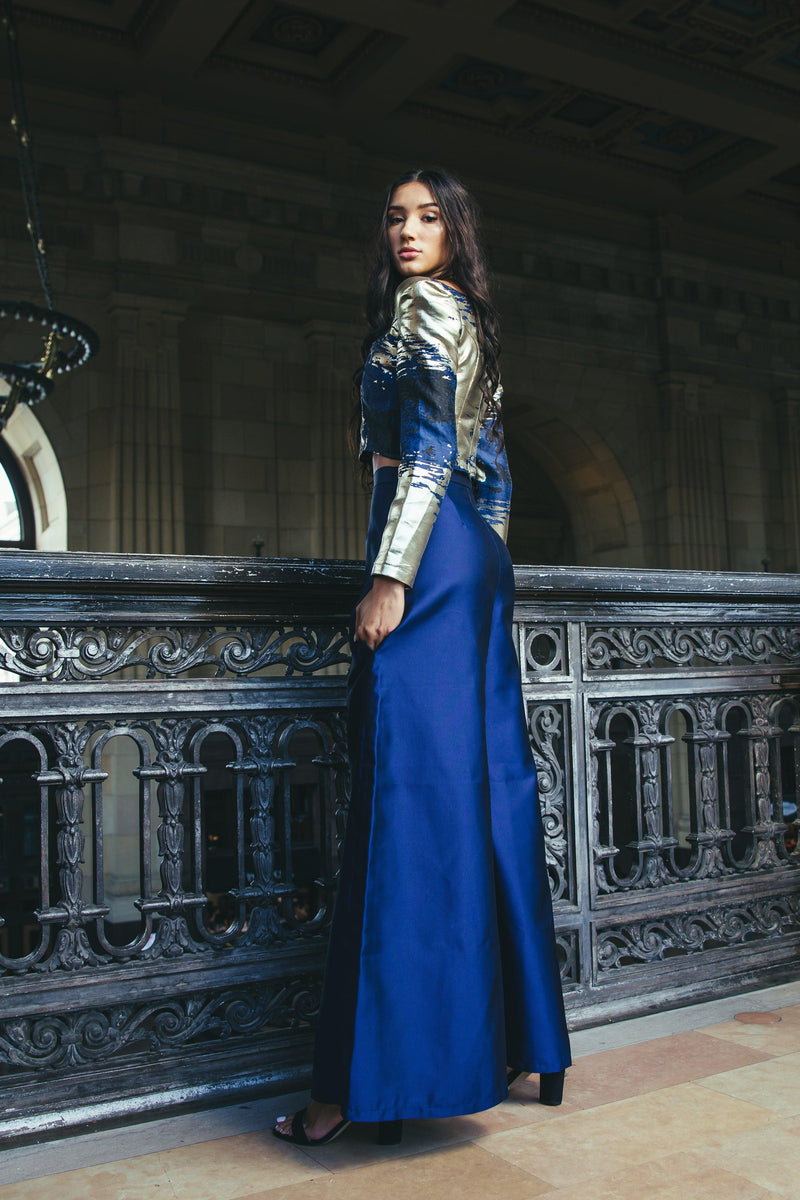 A model posing in the 'Zendaya Top' complemented by a gold jacket, standing by a railing