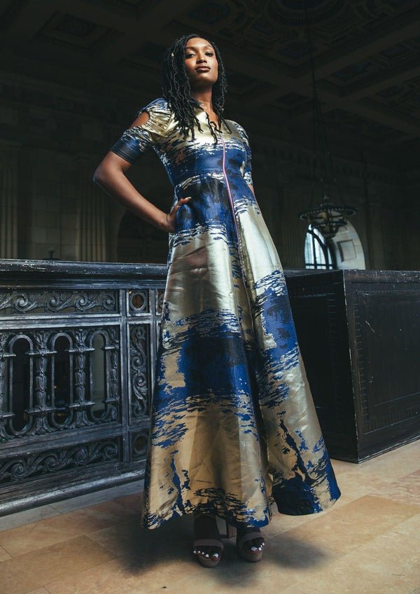 Model showcasing the Cleopatra Maxi Dress with blue and gold patterns in an indoor setting