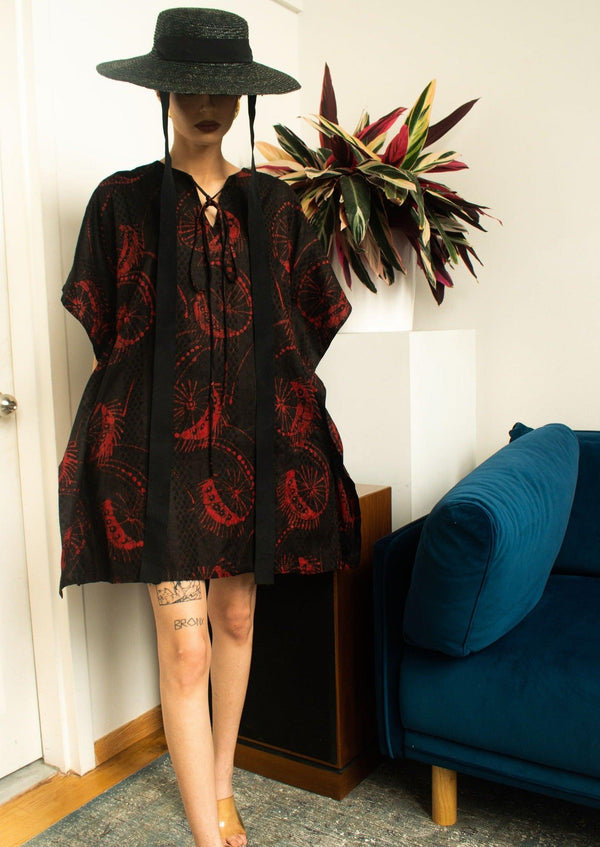 Model wearing Kikuyu Kaftan paired with a black hat, posing in front of a sofa